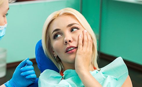 Woman holding cheek in dental chair before emergency dentistry