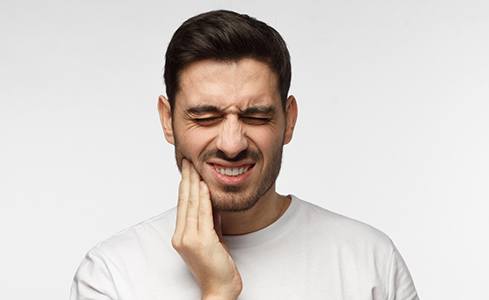A young man holding his cheek as he suffers from a serious toothache before emergency dentistry