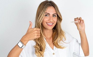 Smiling woman giving thumbs up while holding Invisalign aligner