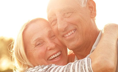 Older man and woman smiling outdoors after one visit dental restorations