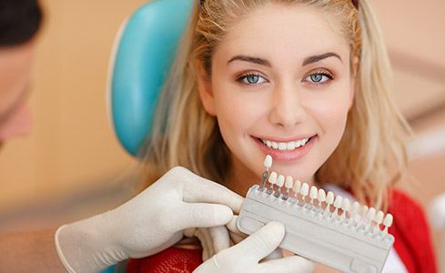 Woman's smile compared with porcelain veneer shades during cosmetic dentistry visit