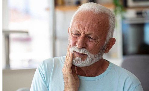 Bearded man sitting on couch with tooth pain