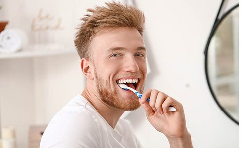Man in bathroom smiling and brushing teeth