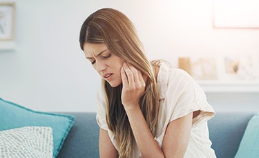 Woman on couch rubbing her jaw in pain