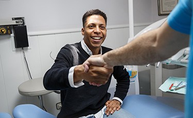 Male dental patient smiling and shaking dentist’s hand