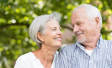 Older couple smiling together after tooth replacement with dental implants