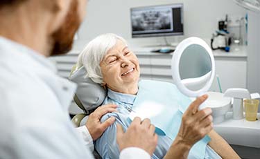 senior dental patient admiring her new smile in a mirror