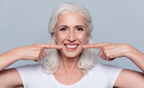 Senior woman pointing to her smile after dental implant supported tooth replacement