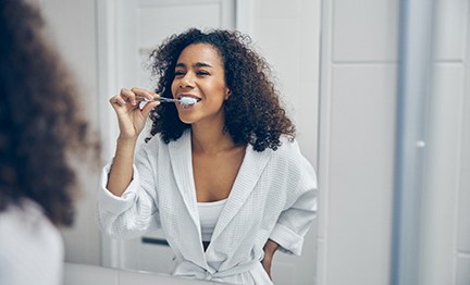 Woman smiling while brushing her teeth in bathroom