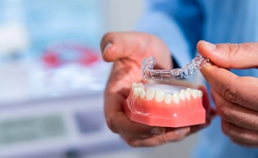 Dentist placing Invisalign aligner on model of teeth