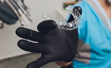 Dentist holding Invisalign aligner with black glove