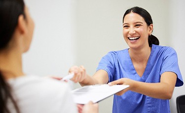 Smiling dental assistant handing patient forms