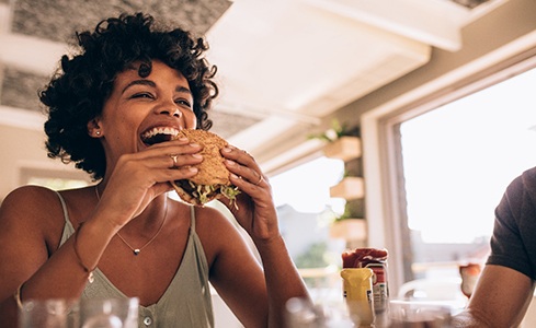 Smiling woman eating burger at restaurant