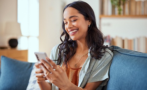 Woman smiling while looking at phone on couch