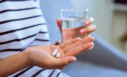 Person in striped shirt holding pills and glass of water