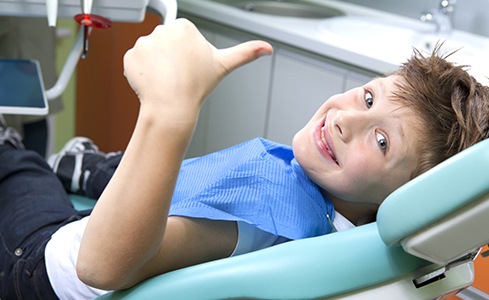 Young boy in dental chair giving thumbs up