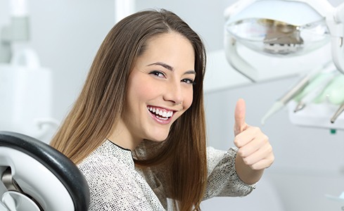 Woman in dental chair giving thumbs up after sedation dentistry treatment