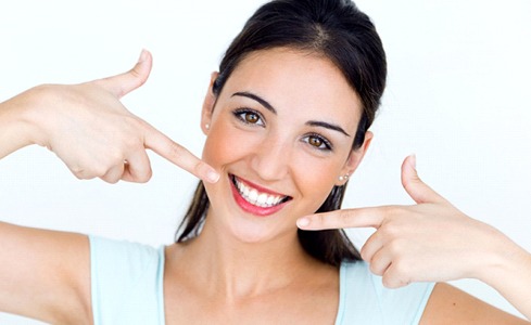 Woman pointing at her bright smile after teeth whitening