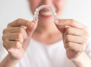 Smiling woman holding out Invisalign in Long Island City