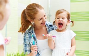 mother showing her daughter how to brush her teeth