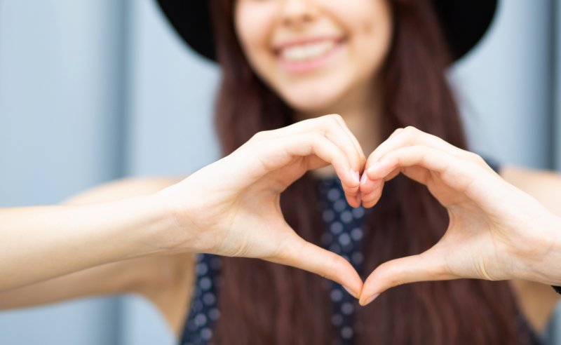 person smiling and making a heart with their hands