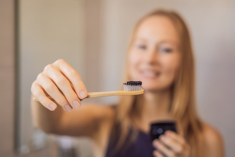 young woman brushing teeth with activated charcoal 