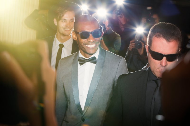 male celebrity with porcelain veneers and sunglasses smiling with bodyguard