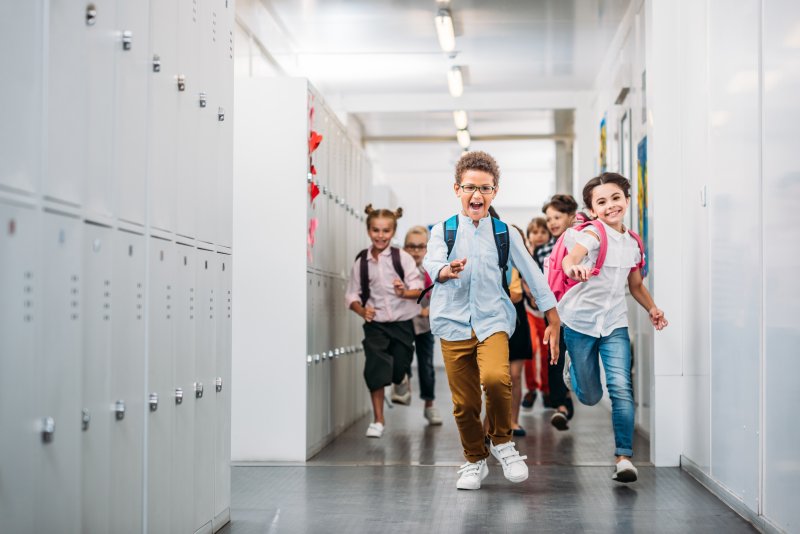 A smiling group of kids running through a school corridor